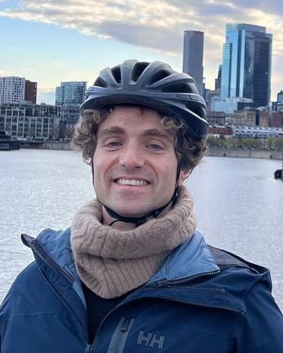 Iulian Serban smiling in a bike helmet, with the Montreal skyline behind him